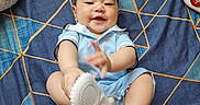 Chadric Ashton is registered to the contest to win money with this photo: baby, bed, bedspread, blue, child, clothing, geometric_pattern, happy, indoors, infant, light_blue_outfit, photography, pillow, playful, portrait, shoes, sitting, smiling, toy, white_shoes