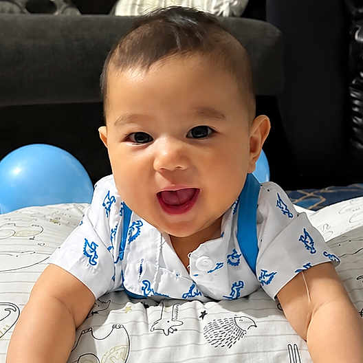 Chadric Ashton is registered to the contest to win money with this photo: baby, child, infant, smiling, laughing, portrait, indoor, bed, bedding, pajamas, blue_balloons, balloon, happy, sitting, lying_down, face, eyes, short_hair, home, cozy
