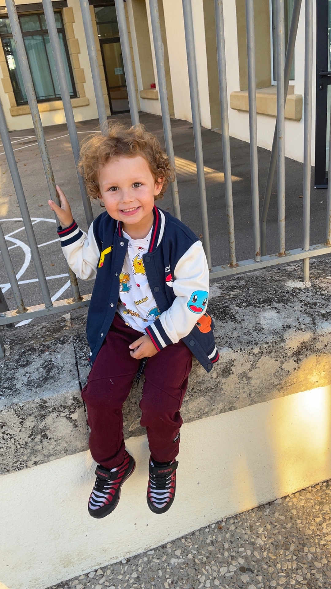 Sandro participe au concours pour gagner de l'argent avec cette photo : child, smiling, curly_hair, jacket, pokemon, sneakers, concrete, metal_bars, outdoor, playground, casual_clothing, person, happy, young, cute, daylight, urban, seated, holding, face