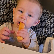 Tony a rejoint le concours — aidez-le/la à gagner de superbes lots ! baby_food, blue_eyes, child, clothing, crumbs, curious, eating, face, hand, high_chair, indoor, light_brown_hair, meal_time, mouth, patterned_chair, person, snack, table, toddler, young_child