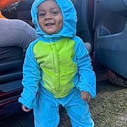 Nakari is registered to the contest to win money with this photo: child, toddler, onesie, costume, dinosaur, smile, dimples, outdoor, grass, car, door, hand, blue, green, clothing, happy, person, footwear, hood, playful