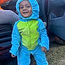 child, toddler, onesie, costume, dinosaur, smile, dimples, outdoor, grass, car, door, hand, blue, green, clothing, happy, person, footwear, hood, playful