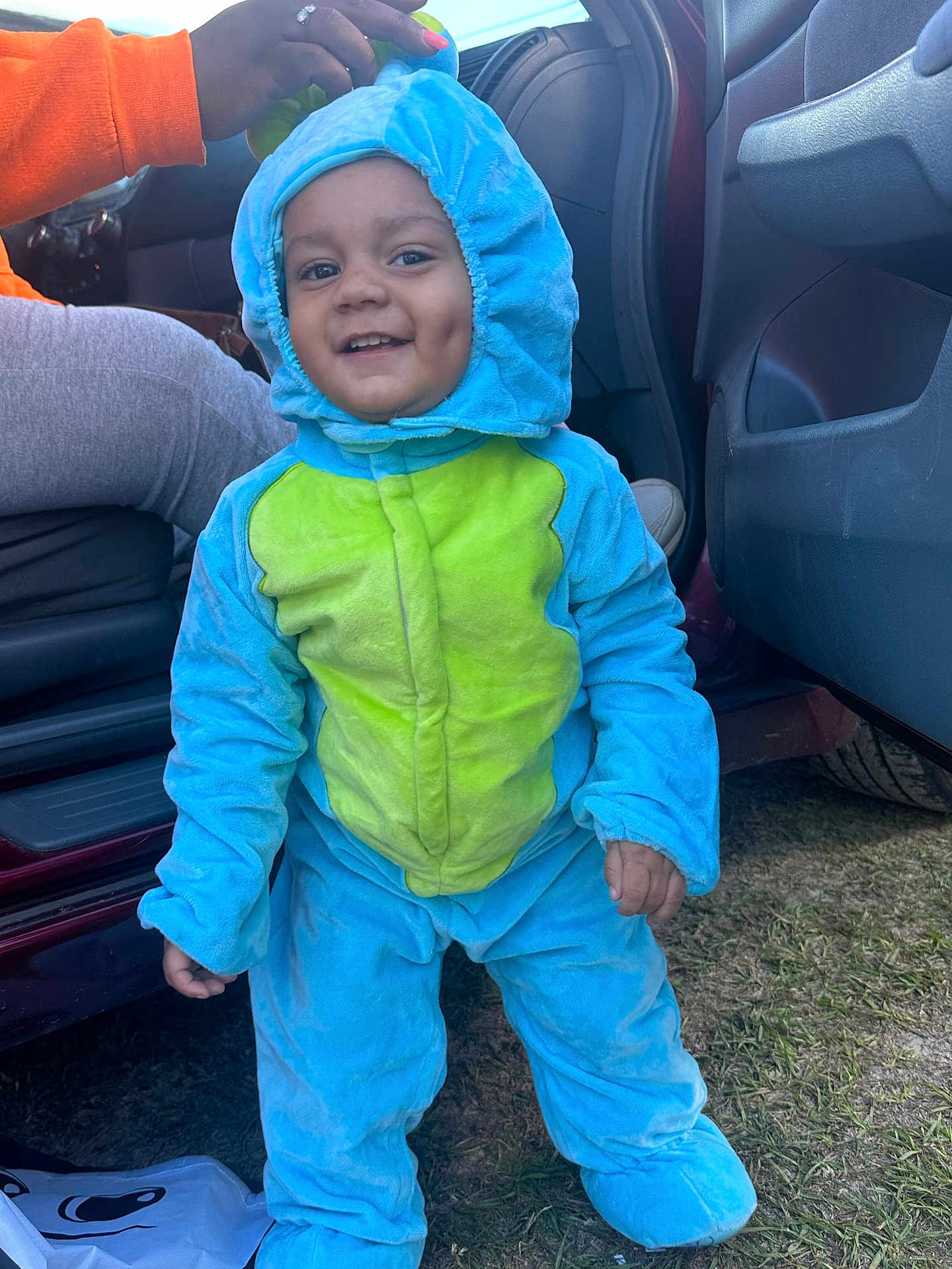 Nakari is registered to the contest to win money with this photo: child, toddler, onesie, costume, dinosaur, smile, dimples, outdoor, grass, car, door, hand, blue, green, clothing, happy, person, footwear, hood, playful