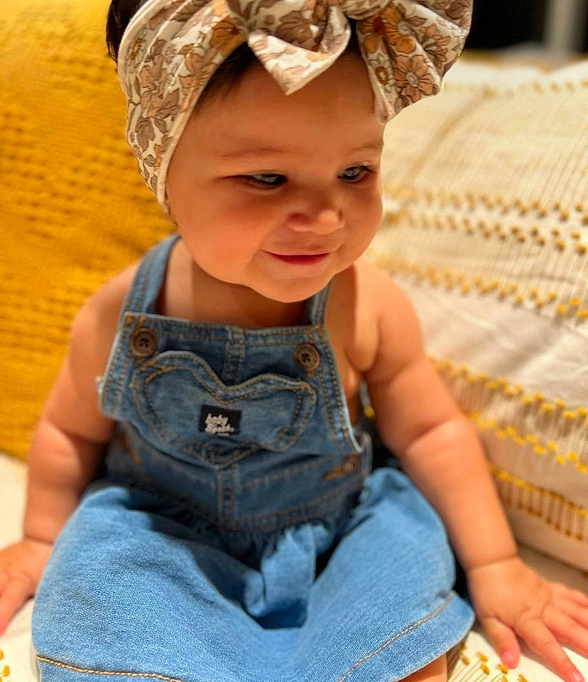 Maggie joined the competition — help win amazing prizes! baby, baby_toddler_clothing, cap, child, clothing, denim, electric_blue, eye, fashion_accessory, grass, happy, headband, headgear, headpiece, headwear, pattern, person, sitting, skin, smile
