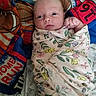 baby, infant, swaddled, blanket, floral_pattern, quilt, sports_theme, face, wide_eyes, fist, bed, bedding, colorful, curious, lying_down, indoors, soft_texture, closeup, person, newborn