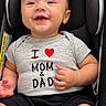 Dylan joined the competition — help win amazing prizes! baby, child, infant, smiling, happy, car_seat, seated, portrait, close_up, face, eyes, short_hair, gray_shirt, black_shorts, text_on_clothing, heart_symbol, thumbs_up, indoor, family, safe