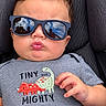 baby, child, infant, sunglasses, pouting, portrait, car_seat, seated, dinosaur, shirt, blue_pants, gray_clothing, hand, face, eyes, hair, indoor, close_up, fashion, cute