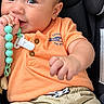 baby, child, infant, car_seat, portrait, smiling, sitting, teething_toy, pacifier_clip, orange_shirt, beige_shorts, brown_hair, blue_eyes, curious, indoors, close_up, face, hands, casual_clothing, photography