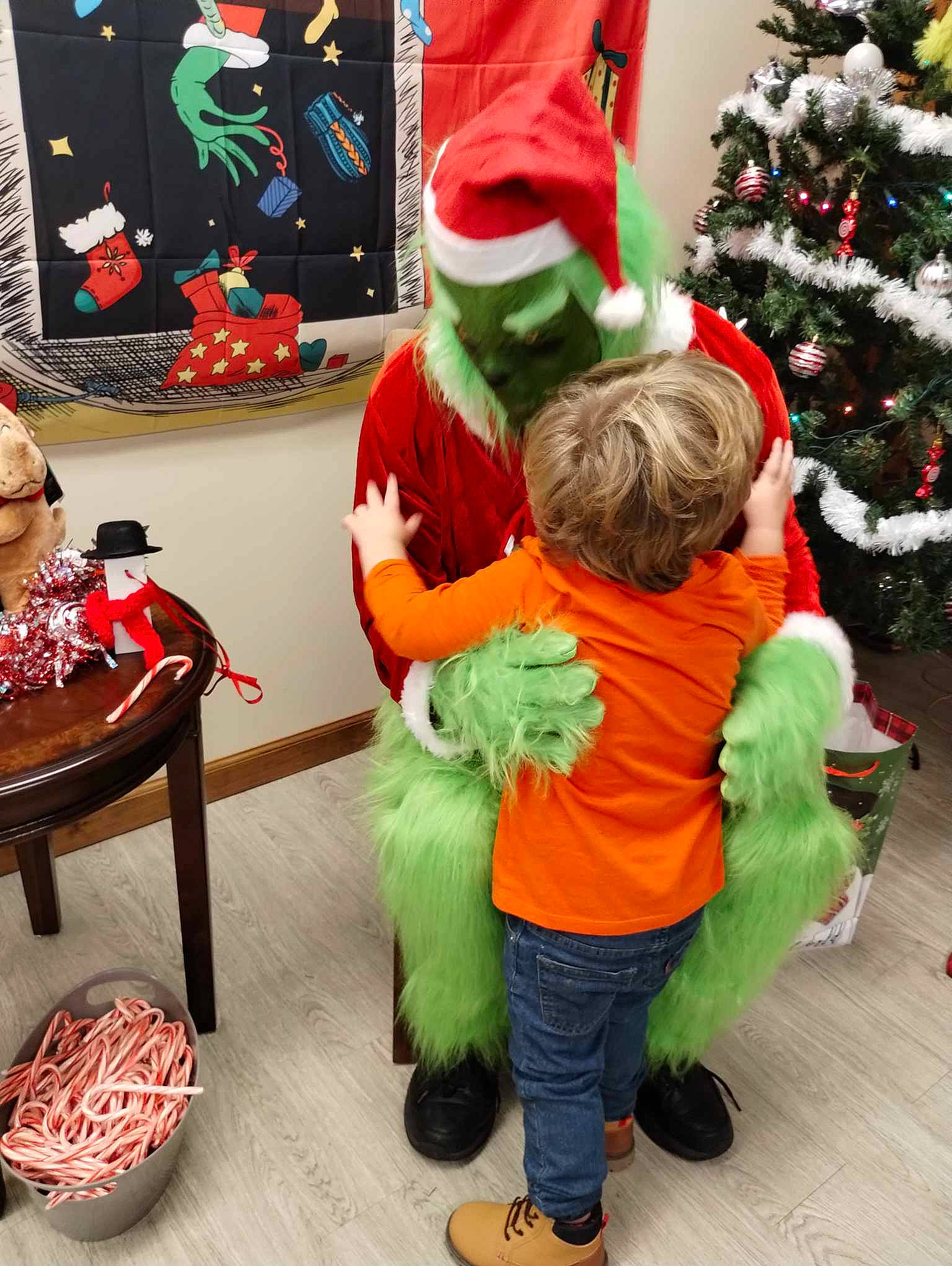 Dereck is registered to the contest to win money with this photo: christmas, christmas_decoration, christmas_eve, christmas_ornament, christmas_tree, costume_hat, event, fictional_character, fun, green, hat, holiday, holiday_ornament, outerwear, person, room, santa_claus, snapshot, table, toddler