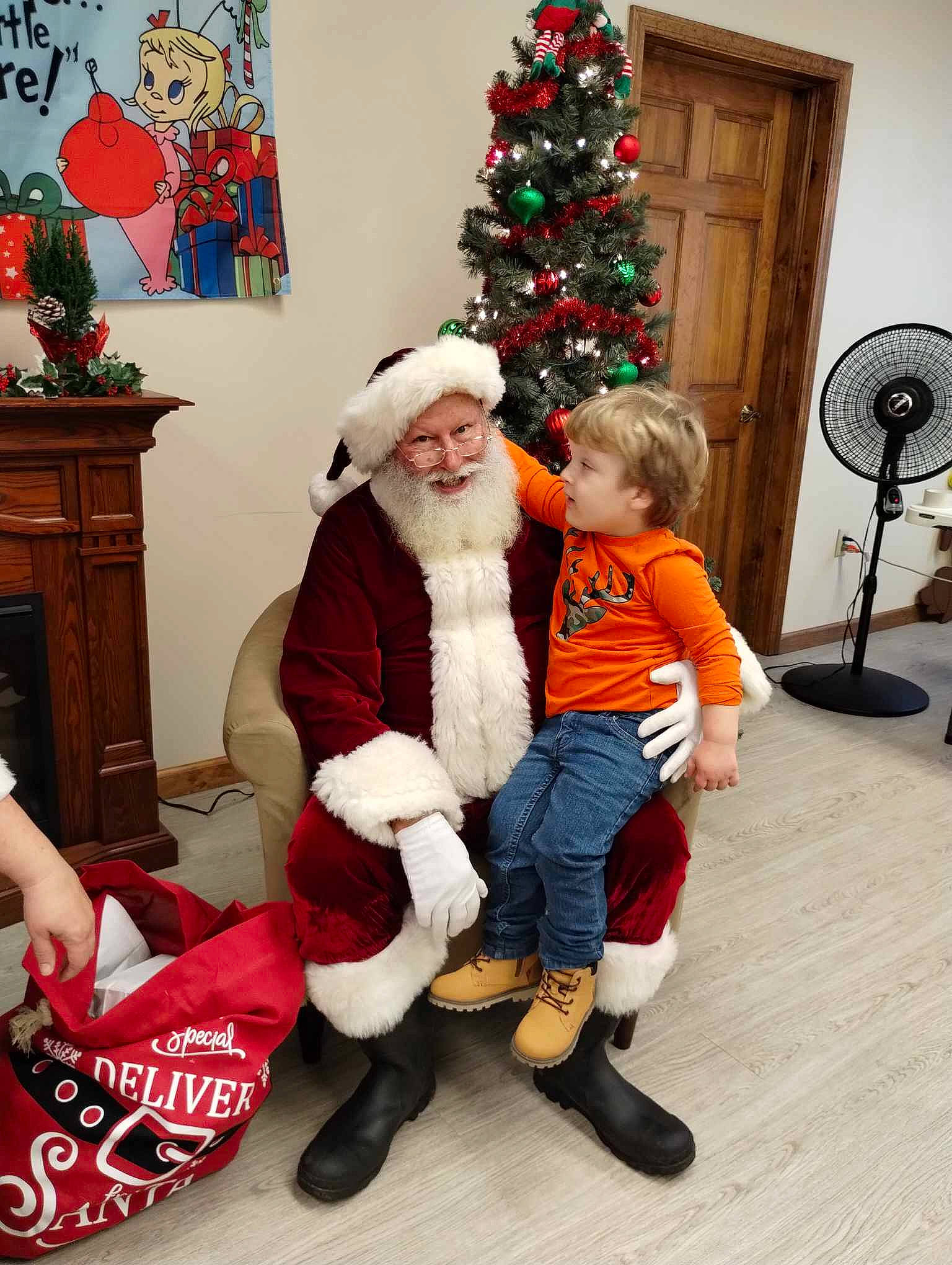 Dereck is registered to the contest to win money with this photo: boot, christmas, christmas_decoration, christmas_ornament, christmas_tree, event, fictional_character, fun, hat, headwear, holiday, holiday_ornament, lap, mechanical_fan, person, red, santa_claus, sitting, smile, standing