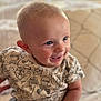 baby, smiling, blue_eyes, cute, shirt, cartoon_print, child, sitting, indoor, cushion, soft_lighting, happy, portrait, close_up, infant, face, skin, cute_expression, young_child, cheerful