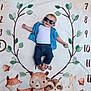 baby, child, sunglasses, denim_shirt, jeans, milestone_blanket, numbers, leaves, woodland_animals, fox, bear, raccoon, rabbit, smiling, lying_down, cute, infant, celebration, blanket, soft_texture