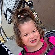 Brexley is registered to the contest to win money with this photo: child, toddler, costume, smile, headband, antennae, outdoor, building, sidewalk, brick_wall, happy, face, hair, pink, black, blue, clothing, window, daylight, person