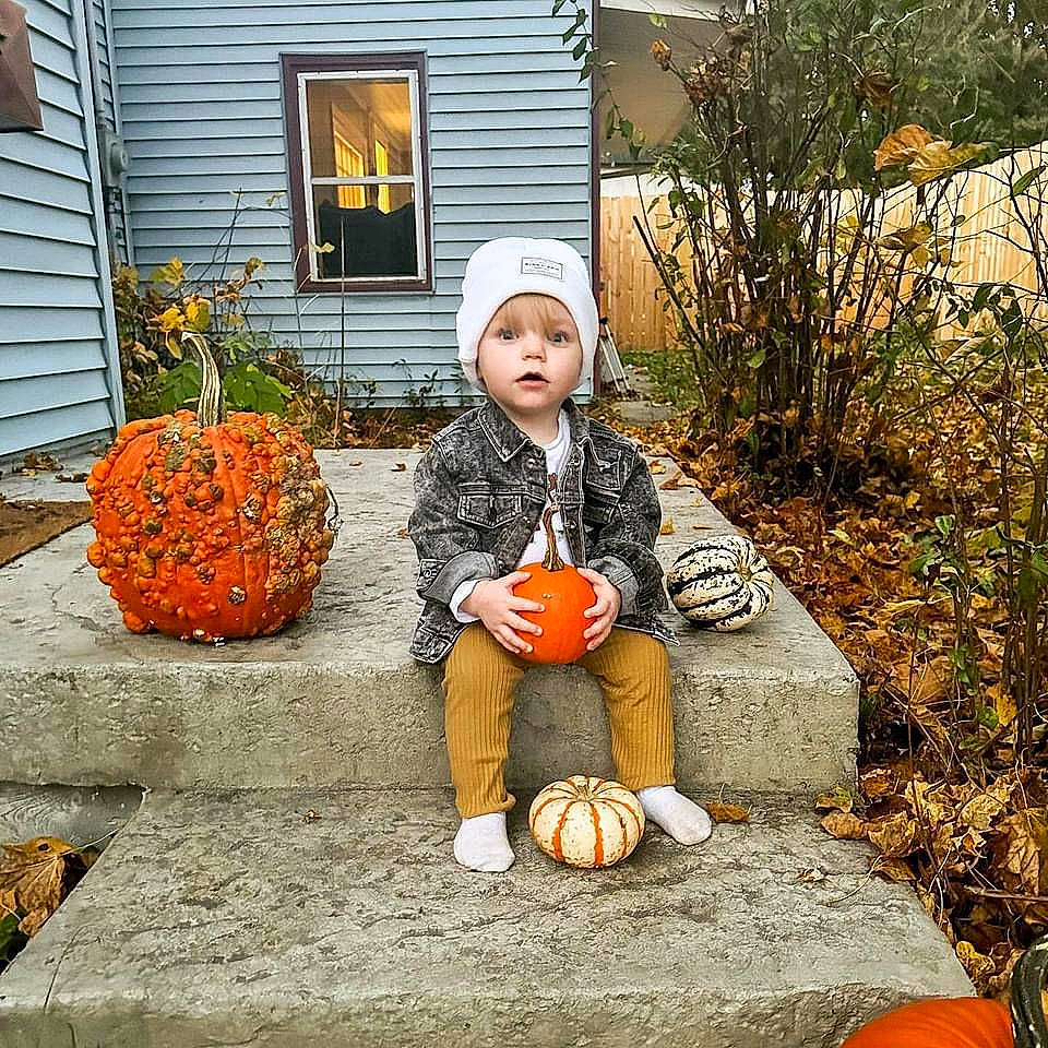 Rowan is registered to the contest to win money with this photo: calabaza, child, cucurbita, flowerpot, garden, gourd, grass, headwear, house, houseplant, natural_foods, orange, people_in_nature, person, plant, pumpkin, sitting, squash, toddler, vegetable