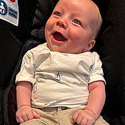 Haydn is registered to the contest to win money with this photo: baby, smiling, infant, car_seat, clothing, white_shirt, sailboat_pattern, beige_pants, happy, cute, child, portrait, blue_eyes, skin, person, sitting, closeup, young_child, casual_wear, infancy