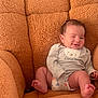 baby, infant, smiling, newborn, onesie, diaper, plush_chair, armchair, cozy, happy, portrait, sitting, indoors, soft_texture, brown, cute, face, feet, toes, family_text