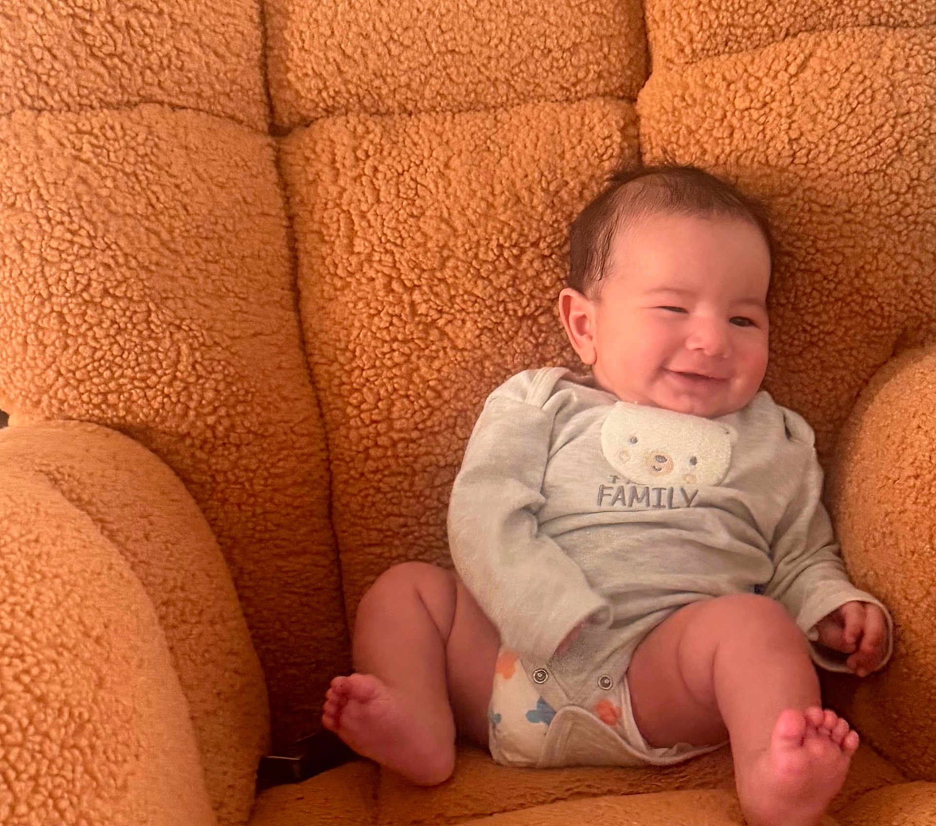 Taim joined the competition — help win amazing prizes! baby, infant, smiling, newborn, onesie, diaper, plush_chair, armchair, cozy, happy, portrait, sitting, indoors, soft_texture, brown, cute, face, feet, toes, family_text