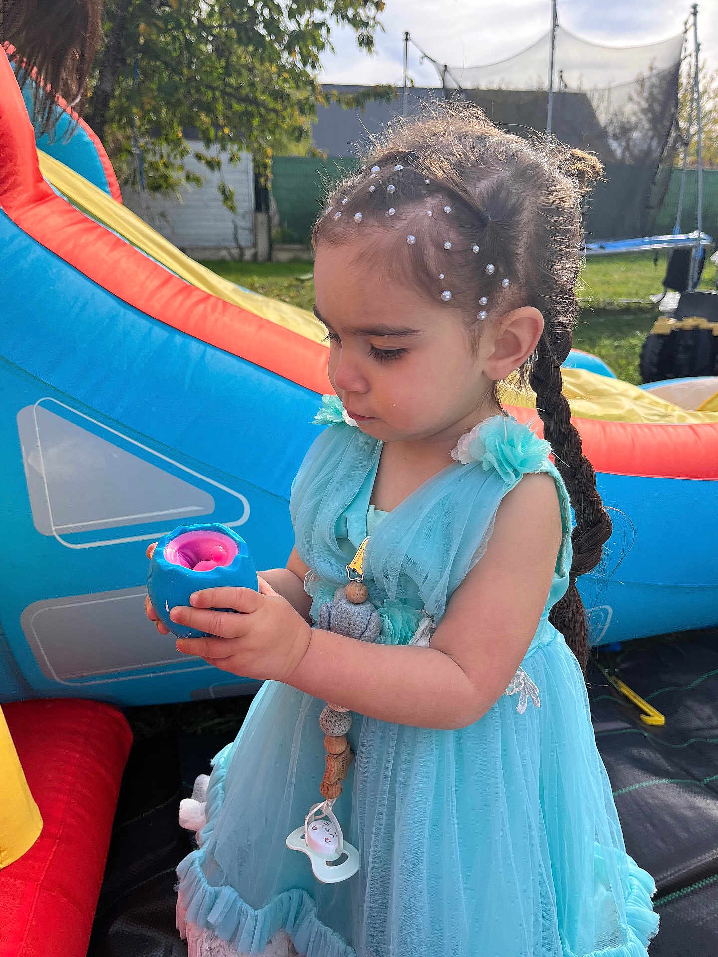 Nina a rejoint le concours — aidez-le/la à gagner de superbes lots ! child, girl, blue_dress, toy, outdoor, playground, inflatable, beaded_hair, curious, daylight, grass, backyard, summer, young_child, portrait, side_view, cute, play, person, casual