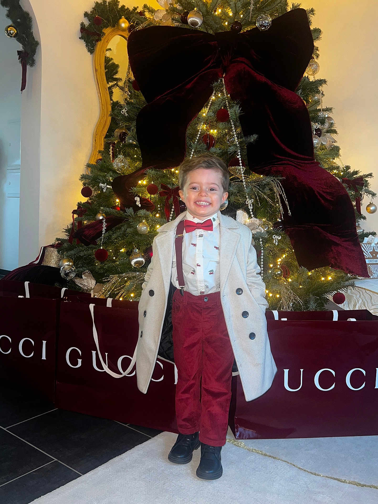 Franck Junior participe au concours pour gagner de l'argent avec cette photo : bow_tie, boy, carpet, celebration, child, christmas_tree, coat, decorations, festive, happy, holiday, indoor, lights, luxury, mirror, pants, shoes, shopping_bags, smiling, suspenders