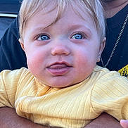 Sawyer is registered to the contest to win money with this photo: adult, arm, baby, blonde_hair, blue_eyes, child, close_up, curious, cute, expression, face, holding, infant, necklace, outdoor, person, portrait, shirt, skin, yellow_clothing