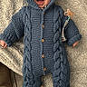 baby, blue_knitted_onesie, hood, smiling, pacifier_clip, blanket, floor_tiles, boots, happy, infant, cozy, indoor, child, clothing, person, cute, portrait, warm, home, comfort