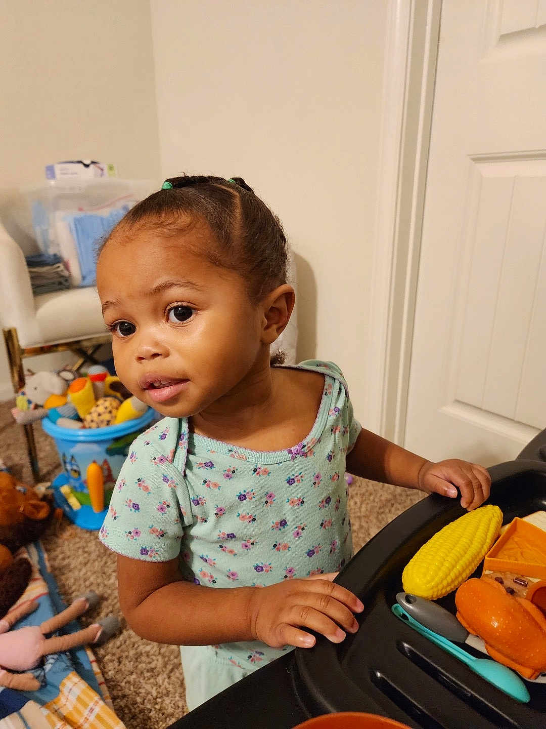 Halo joined the competition — help win amazing prizes! toddler, child, toy_food, play_table, braided_hair, curious_expression, floral_shirt, indoor, carpet, chair, bucket, stuffed_animals, doll, door, hand, face, person, playing, room, home