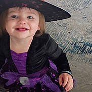 Julia joined the competition — help win amazing prizes! child, toddler, witch_costume, purple_dress, witch_hat, smiling, portrait, indoor, home, carpet, rug, furniture, costume, halloween, happy, face, person, sitting, phone_screenshot, photography