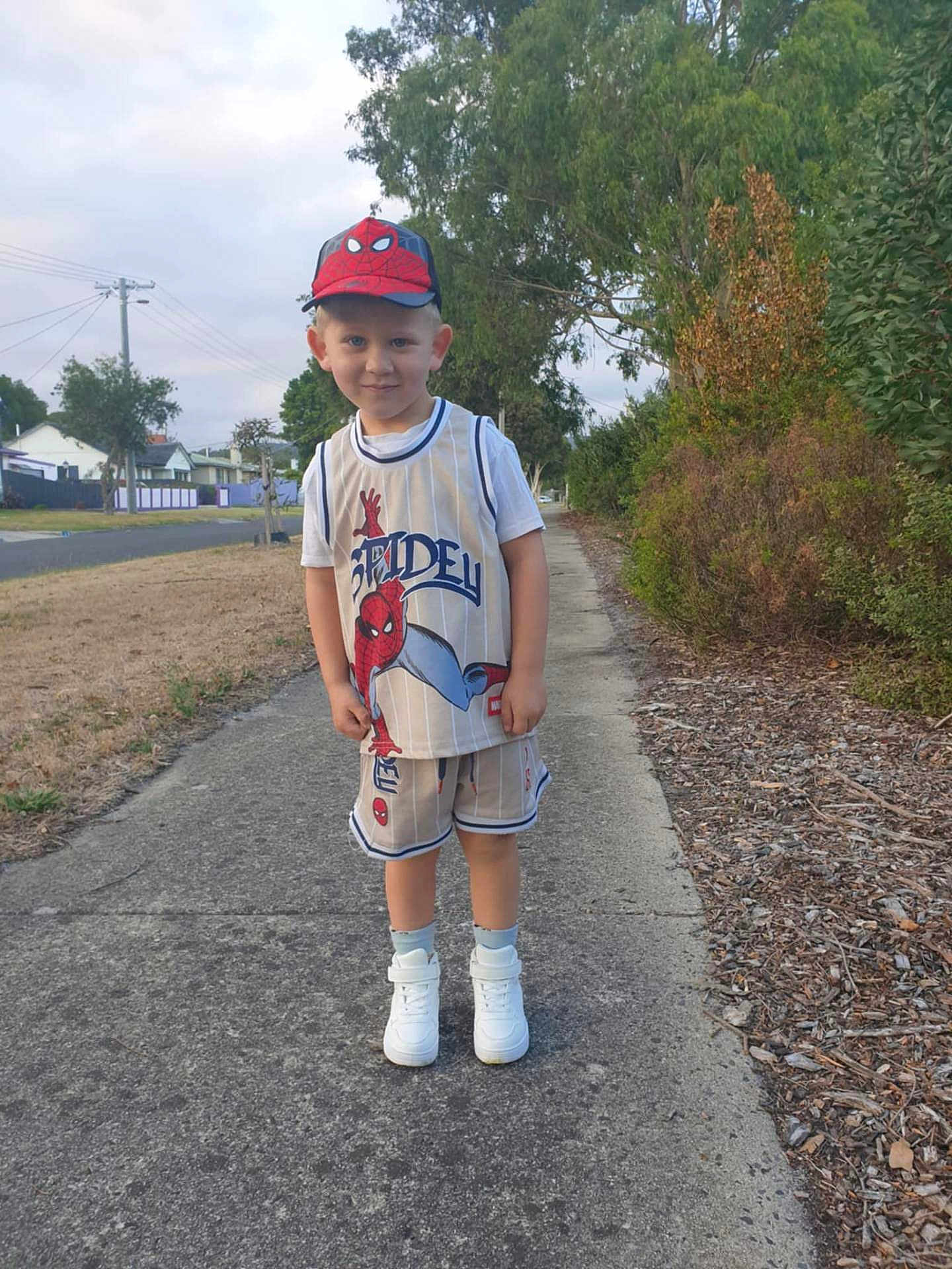 Cruze is registered to the contest to win money with this photo: child, boy, spiderman, cap, shorts, sneakers, sidewalk, outdoor, trees, grass, residential_area, smile, pose, street, daylight, casual_clothing, person, nature, happy, summer