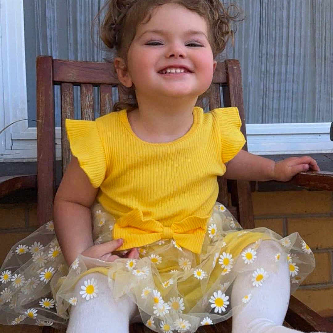 Mackenzie-Lee is registered to the contest to win money with this photo: child, toddler, smiling, yellow_dress, daisies, white_tights, wooden_chair, outdoor, happy, cute, portrait, sitting, playful, girl, clothing, window, background, hair, fun, dirt