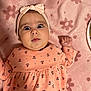 baby, baby_hand, bow, child, cute, face, floral_dress, headband, indoors, infant, laying_down, patterned_clothing, pink_blanket, portrait, skin, soft_texture, surprised_expression, toddler, wide_eyes, young_child