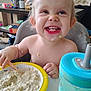 toddler, child, oatmeal, high_chair, food, smiling, face, messy, sippy_cup, table, spoon, kitchen, indoor, person, breakfast, baby_food, happy, meal, plastic_bowl, cute