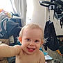 baby, child, smiling, blue_eyes, bare_chest, indoor, floor, clutter, bag, shoe, curtain, wooden_floor, person, happy, portrait, young_child, playful, messy_room, light, hair