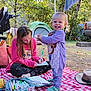 child, toddler, outdoor, camping, tent, markers, drawing, blanket, smile, nature, trees, toy, hat, clothing, person, grass, daylight, parked_vehicle, recreation, leisure