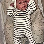 baby, infant, onesie, striped_clothing, headband, bow, cushion, crib, blanket, sleeping_area, face, person, newborn, cute, resting, cozy, indoors, child, wrapped, soft_fabric