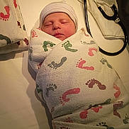 Jaxson is registered to the contest to win money with this photo: newborn, baby, swaddled, blanket, hospital, footprints, hat, sleeping, infant, medical, stethoscope, bed, peaceful, cute, wrapped, face, headwear, person, indoors, soft
