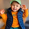 toddler, child, smiling, happy, cap, baseball_cap, vest, puffy_vest, orange_shirt, teal_pants, sitting, raised_hands, indoor, portrait, cute, young_child, person, clothing, face, joyful