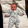 baby, infant, onesie, floral_pattern, white_towel, lying_down, curious_expression, wide_eyes, newborn, soft_texture, fabric, cute, small_hands, sleepwear, indoors, child, person, portrait, resting, cozy