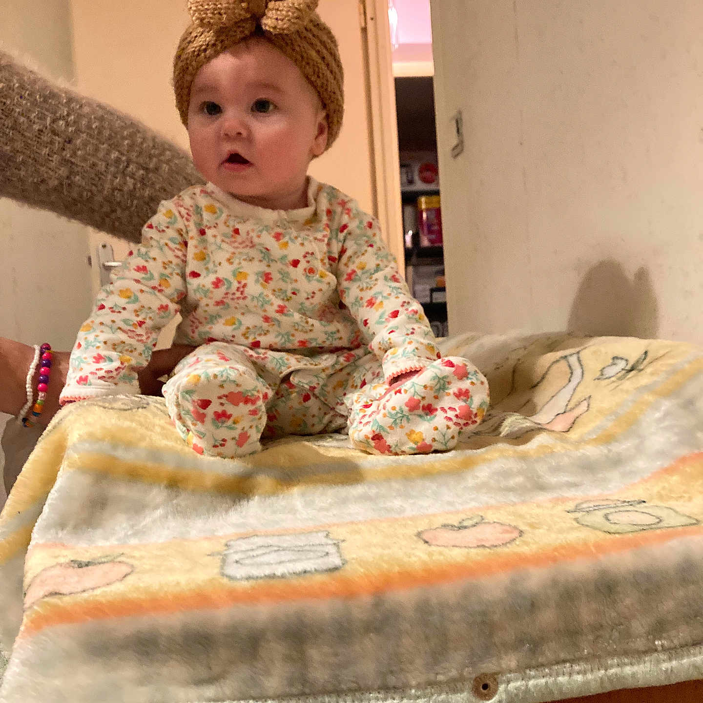 Katalina participe au concours pour gagner de l'argent avec cette photo : arm, baby, blanket, bow, child, curious, doorway, hand, indoor, knitted_headband, long_sleeve_pajamas, pantry, patterned_clothing, person, sitting, soft_texture, storage, warm_colors, wide_eyes, wooden_surface