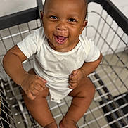 Malik joined the competition — help win amazing prizes! baby, shopping_cart, smiling, happy, infant, white_onesie, skin, hair, metal, grid, floor_tiles, shopping, cute, child, sitting, barefoot, expressive_face, indoor, person, joy
