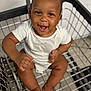 baby, shopping_cart, smiling, happy, infant, white_onesie, skin, hair, metal, grid, floor_tiles, shopping, cute, child, sitting, barefoot, expressive_face, indoor, person, joy