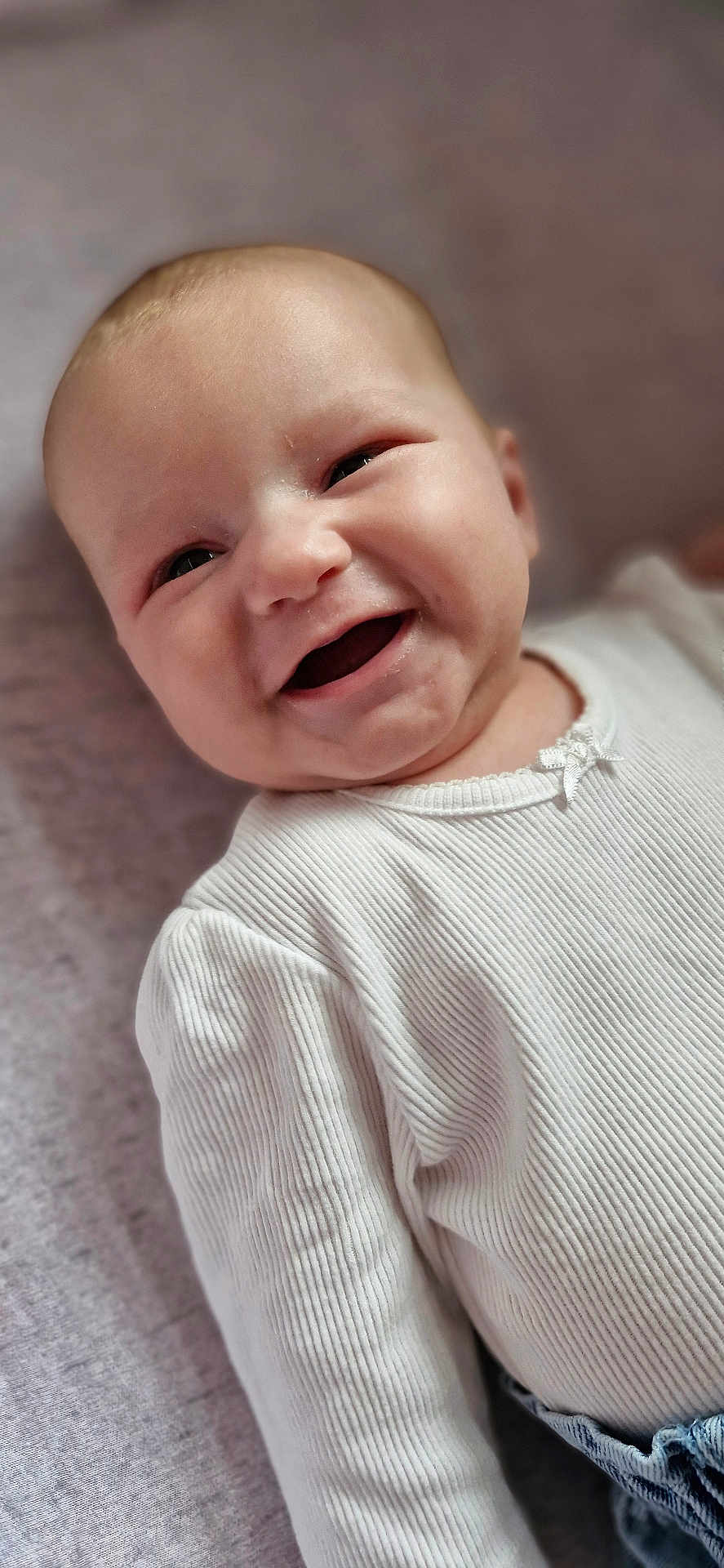 Adah-Jayne is registered to the contest to win money with this photo: baby, infant, smiling, white_shirt, ribbed_clothing, closeup, face, cute, joyful, happy, child, portrait, soft_background, lying_down, indoor, skin, head, eyes, mouth, expression