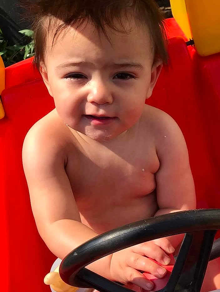 Mason joined the competition — help win amazing prizes! toddler, child, toy_car, steering_wheel, outdoor, sunlight, red, yellow, skin, hands, face, hair, expression, play, summer, daylight, cute, young, person, vehicle