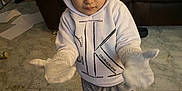 Messiah is registered to the contest to win money with this photo: toddler, child, hoodie, mittens, beanie, indoor, floor, tiles, couch, blanket, paper, paper_towels, clothing, footwear, person, young_child, curious, warm_clothing, home, casual
