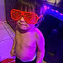 Messiah is registered to the contest to win money with this photo: toddler, child, glasses, red_glasses, shutter_shades, shirtless, diaper, black_pants, purple_light, indoor, tile_floor, cabinet, paper_towel, standing, expression, young_child, person, face, hair, lighting