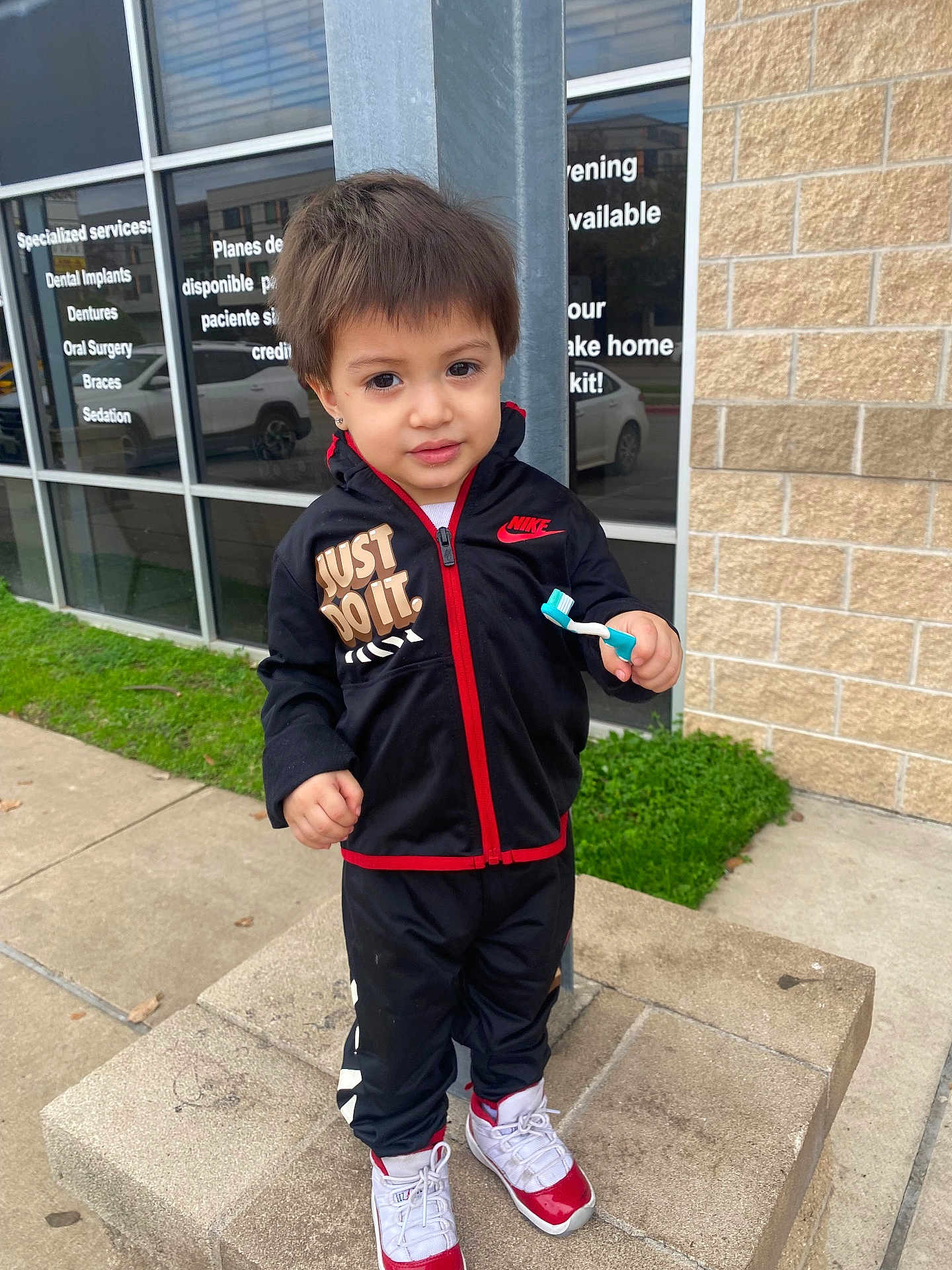 Messiah joined the competition — help win amazing prizes! child, boy, tracksuit, nike, toothbrush, concrete, sidewalk, building, window, brick_wall, grass, sneakers, outdoor, casual_clothing, person, young_child, curious, standing, urban, daytime