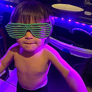 Messiah is registered to the contest to win money with this photo: child, glasses, green_glasses, shirtless, indoor, party_lights, purple_lighting, tile_floor, trash_bin, paper_plate, young_child, pose, playful, person, face, hair, short_hair, floor, container, lighting