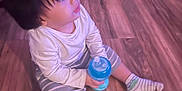 Zayden is registered to the contest to win money with this photo: child, toddler, floor, wooden_floor, sitting, sippy_cup, blue_cup, striped_shorts, long_sleeve_shirt, socks, indoors, curious, young_child, baby, person, casual_clothing, flooring, cute, young_person, portrait
