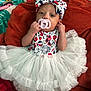 baby, infant, pacifier, headband, bow, tutu, dress, blanket, patterned_clothing, red, white, blue, lying_down, cute, small_hands, indoor, fabric, colorful, soft_texture, person