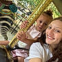 Leigha joined the competition — help win amazing prizes! child, woman, carousel, golden_pole, zebra_statue, outdoor, trees, daylight, smile, selfie, curly_hair, white_tshirt, pink_dress, amusement_ride, playful, park, fence, holding, face, happy