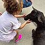 Leigha is registered to the contest to win money with this photo: child, toddler, animal, goat, petting, curly_hair, pink_shoes, white_clothing, concrete, outdoor, adult, kneeling, interaction, casual, daylight, animal_care, human_animal_bond, cute, nature, playful